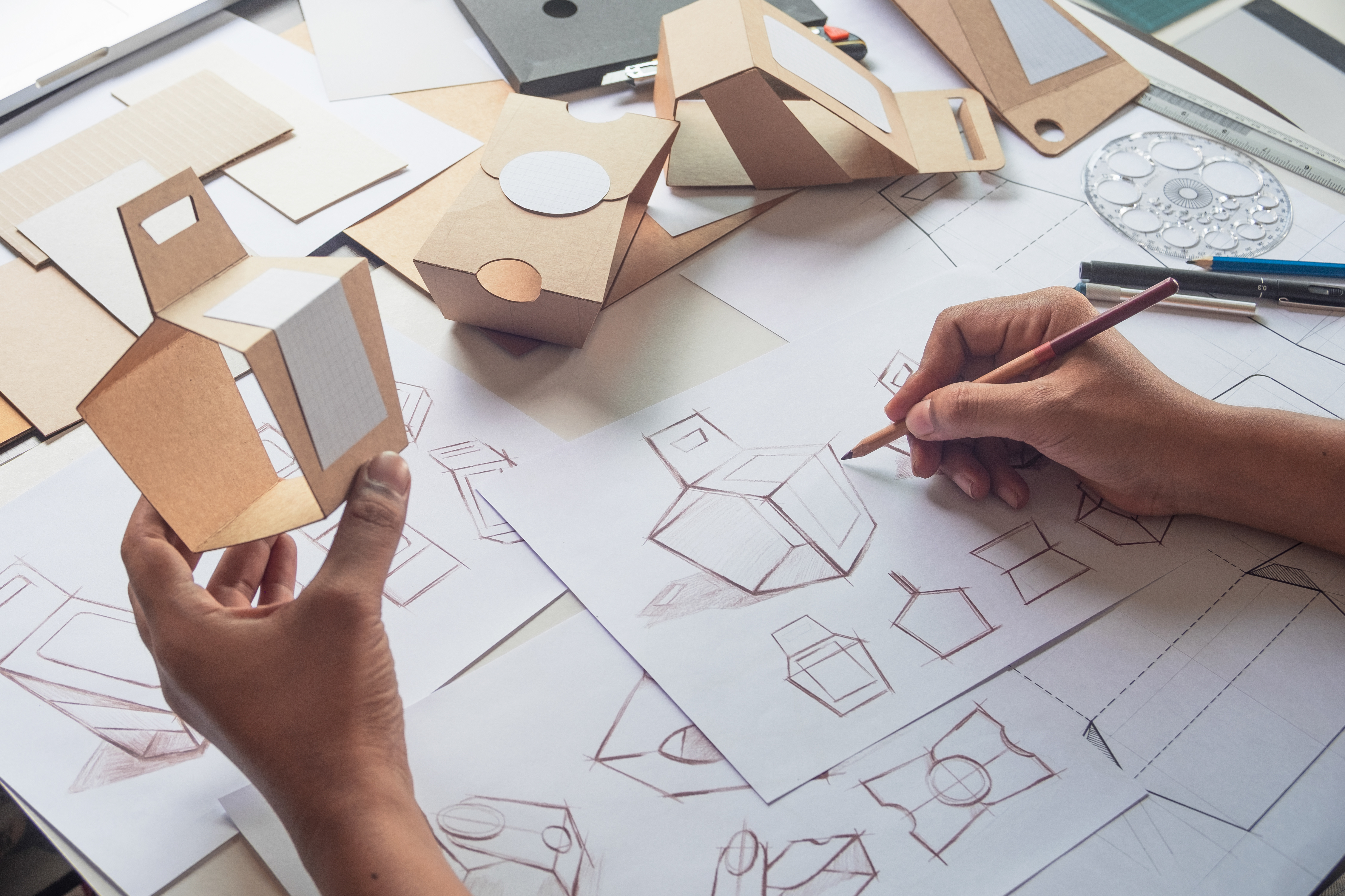 Product designer draws a concept for a new box while holding a working model of the box